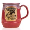 The front of the Bones Coffee Company Coco Crush hand thrown Mug. It has the art for Coco Crush on the golden medallion. The mug is a dark magenta color and has a lavender white glaze on top of it.