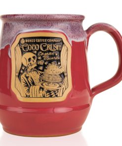 The front of the Bones Coffee Company Coco Crush hand thrown Mug. It has the art for Coco Crush on the golden medallion. The mug is a dark magenta color and has a lavender white glaze on top of it.