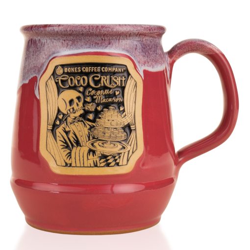 The front of the Bones Coffee Company Coco Crush hand thrown Mug. It has the art for Coco Crush on the golden medallion. The mug is a dark magenta color and has a lavender white glaze on top of it.