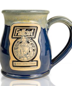 The front of the Bones Coffee Company Lucy hand thrown mug with the Atomic Apple art on the golden medallion. It is inspired by Zenimax and Amazon’s Fallout show. The mug is powder blue colored with a white and yellow glaze on top.
