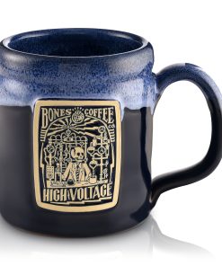 The front of the Bones Coffee Company High Voltage hand thrown mug with the High Voltage coffee art on the golden medallion. The mug is black colored with a blue glaze on top.