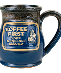 The front of the Bones Coffee Company Coffee First Handthrown Mug. It has the phrase “Coffee first, your nonsense second” on the golden medallion. The mug is federal blue colored with a cinnamon and white glaze.