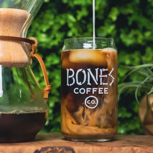 A cold brew glass that has the Bones Coffee Company logo that has the words Bones Coffee Co with the word Bones spelled out with bones. There is coffee inside the cold brew glass.
