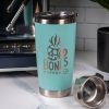 A robin’s egg blue tumbler is on top of a marble surface with an espresso machine and cup behind it. On the tumbler is the Skull Logo for Bones Coffee Company that has a skull that looks like a mug on it.