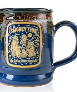 The front of the Bones Coffee Company S’morey Time Handthrown Mug. It has the S’morey Time art on the golden medallion. The mug is blue colored with a cinnamon and white glaze.