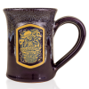 The front of the Bones Coffee Company Bananas Foster Handthrown Mug. It has the art for Bananas Foster coffee on the golden medallion. The mug is a deep purple color and has a banana and white glaze on top of it.