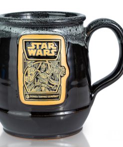 The front of the Bones Coffee Company Dark Side Chocolate Truffle hand thrown mug with the Dark Side Chocolate Truffle coffee art on the golden medallion. The mug is black colored with a white glaze on top. It is inspired by Lucasfilm’s Star Wars.