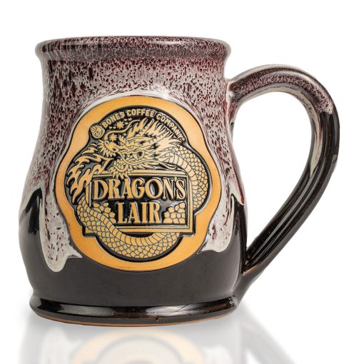 The front of the Bones Coffee Company Dragon’s Lair hand thrown mug with the Dragon’s Lair art on the golden medallion. The mug is black colored with a burgundy and white glaze on top.