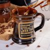 The front of the Bones Coffee Company Murder Hornet Handthrown Mug. It has a hornet with a knife and it says coffee makes me feel less murdery on the golden medallion. The mug is black colored with a sunset orange glaze. There are coffee beans near the mug on a marble surface.