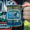 The Coffee First handthrown mug. It is being held up.