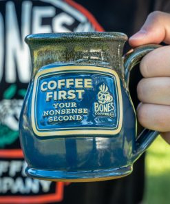 The Coffee First handthrown mug. It is being held up.