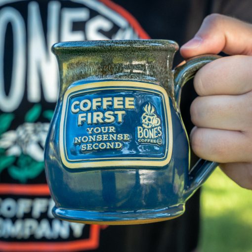 The Coffee First handthrown mug. It is being held up.