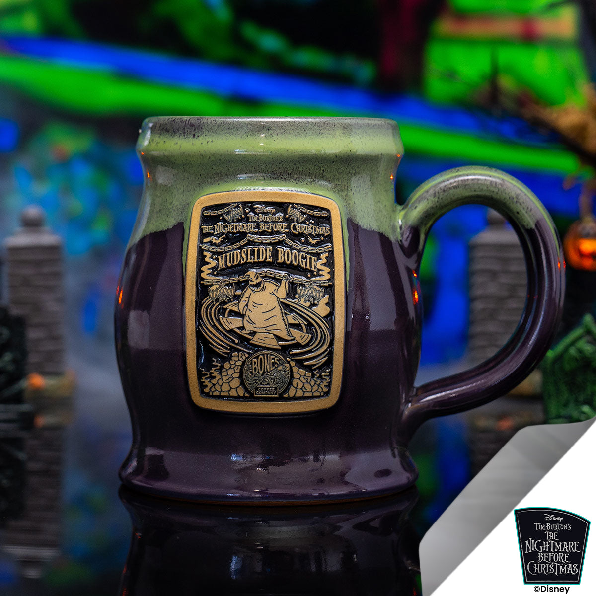 The front of the Bones Coffee Company Mudslide Boogie hand thrown mug with Oogie Boogie on the golden medallion. It is inspired by Disney Tim Burton’s The Nightmare Before Christmas. The mug is plum colored with a kiwi green glaze on top. It is inside a toy graveyard.