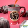 The front of the Bones Coffee Company Souffle Symphony hand thrown mug with Squidward and Plankton on the golden medallion. It is inspired by SpongeBob Squarepants. The mug is cosmo pink colored and has a teal and white glaze on top of it. It has chocolate souffles nearby.