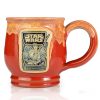 The front of the Bones Coffee Company Twin Sun Tiramisu hand thrown mug with the Twin Sun Tiramisu coffee art on the golden medallion. The mug is paprika colored with a yellow glaze on top. It is inspired by Lucasfilm’s Star Wars.